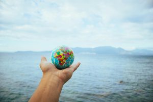 A hand holds a small globe with a scenic ocean backdrop, symbolizing global exploration.